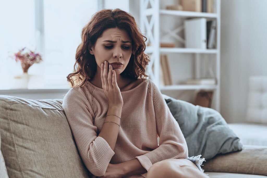 Women sitting on a chair in pain holding her mouth with her hand.