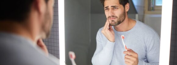 Sad man getting bad tooth ache in mirror brushing teeth