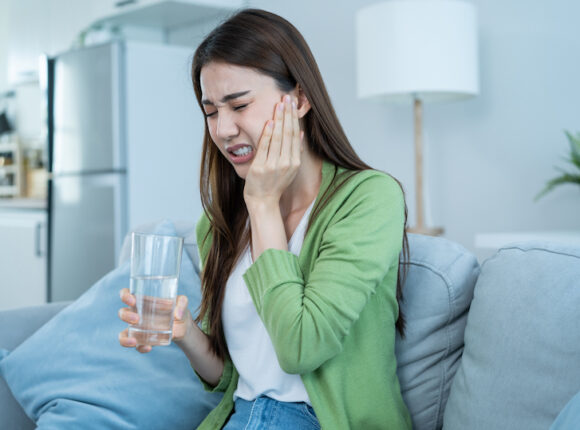 Women in green on a couch experiencing tooth pain while holding a glass of water